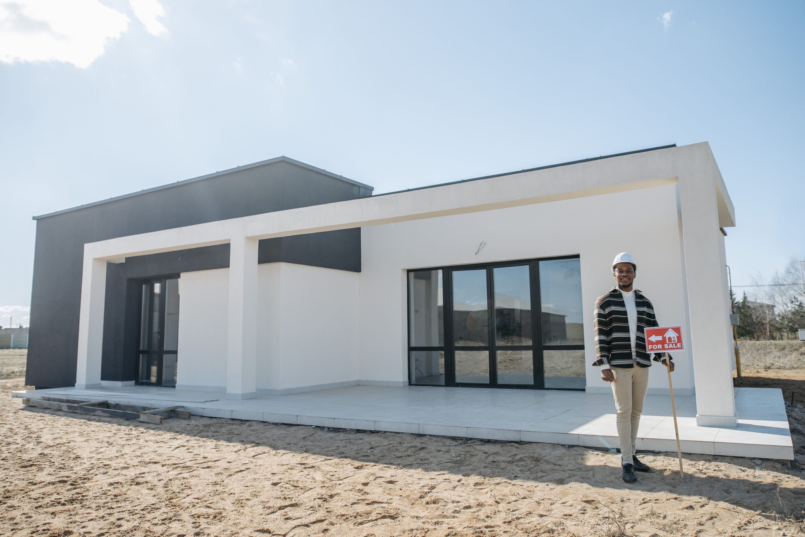 A realtor stands with a for sale sign in front of a modern house.